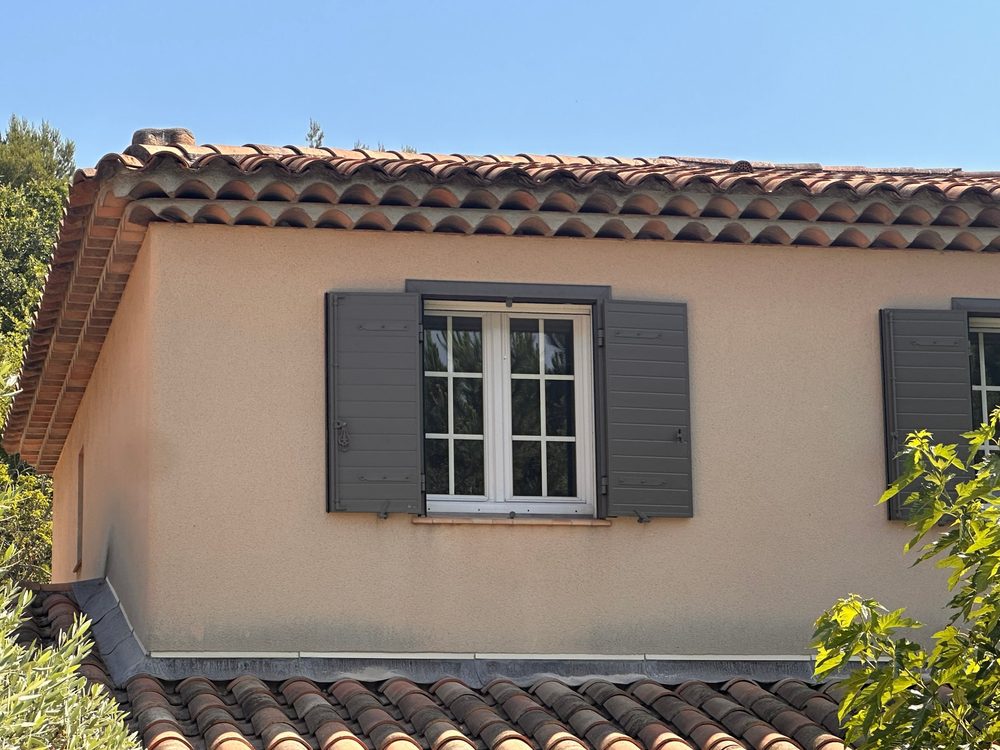 Fenêtre encadrée de volets battants gris sur une façade beige