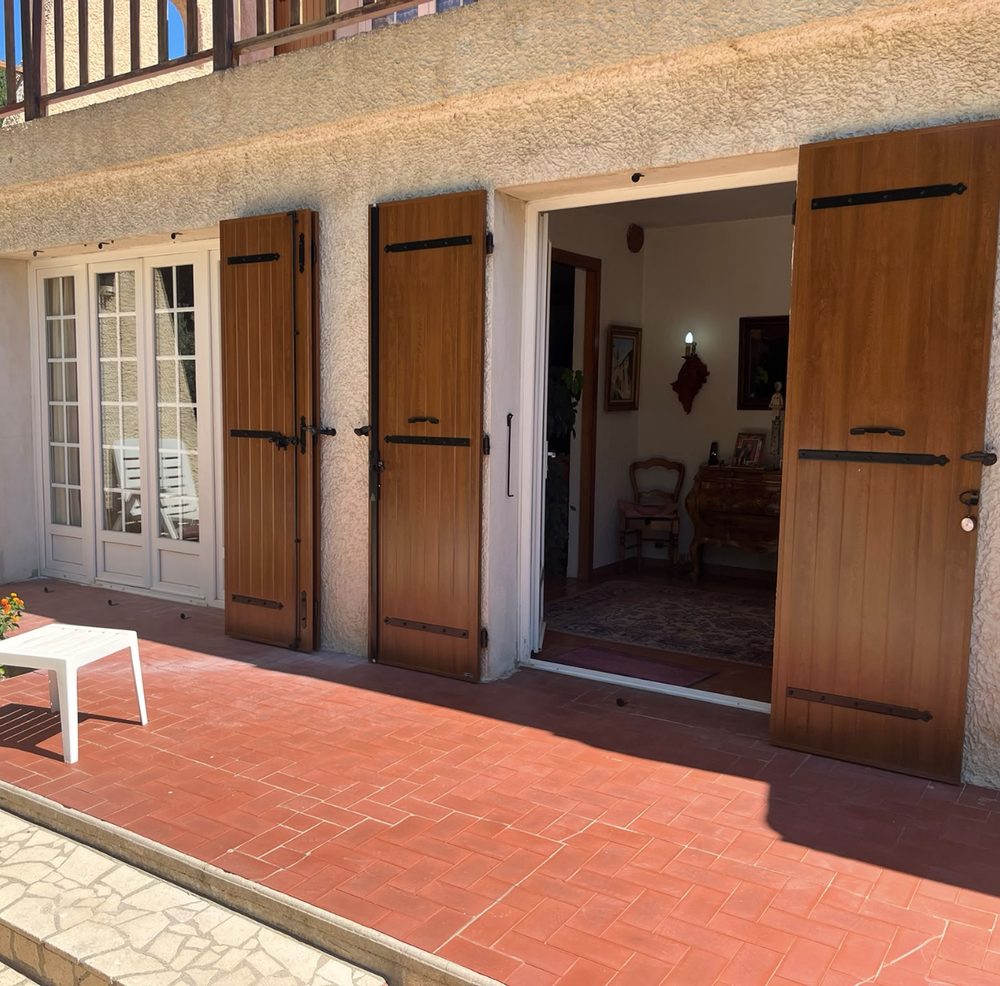 Volets battants marron de chaque côté d’une porte-fenêtre ouverte