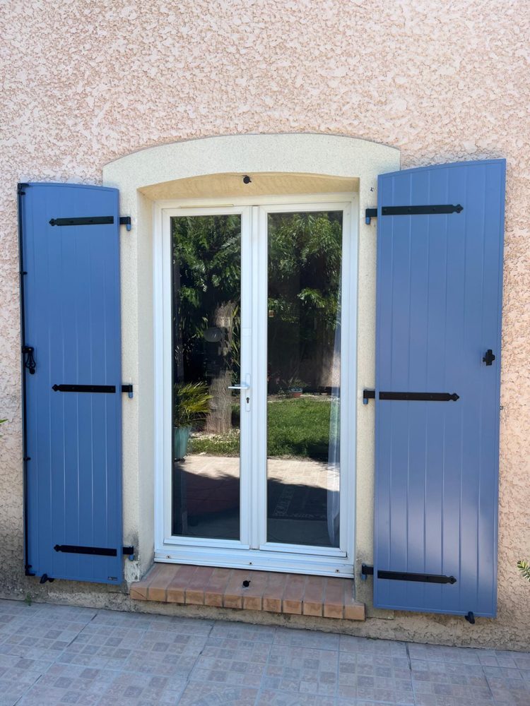 Porte-fenêtre blanche encadrée de volets battants bleus